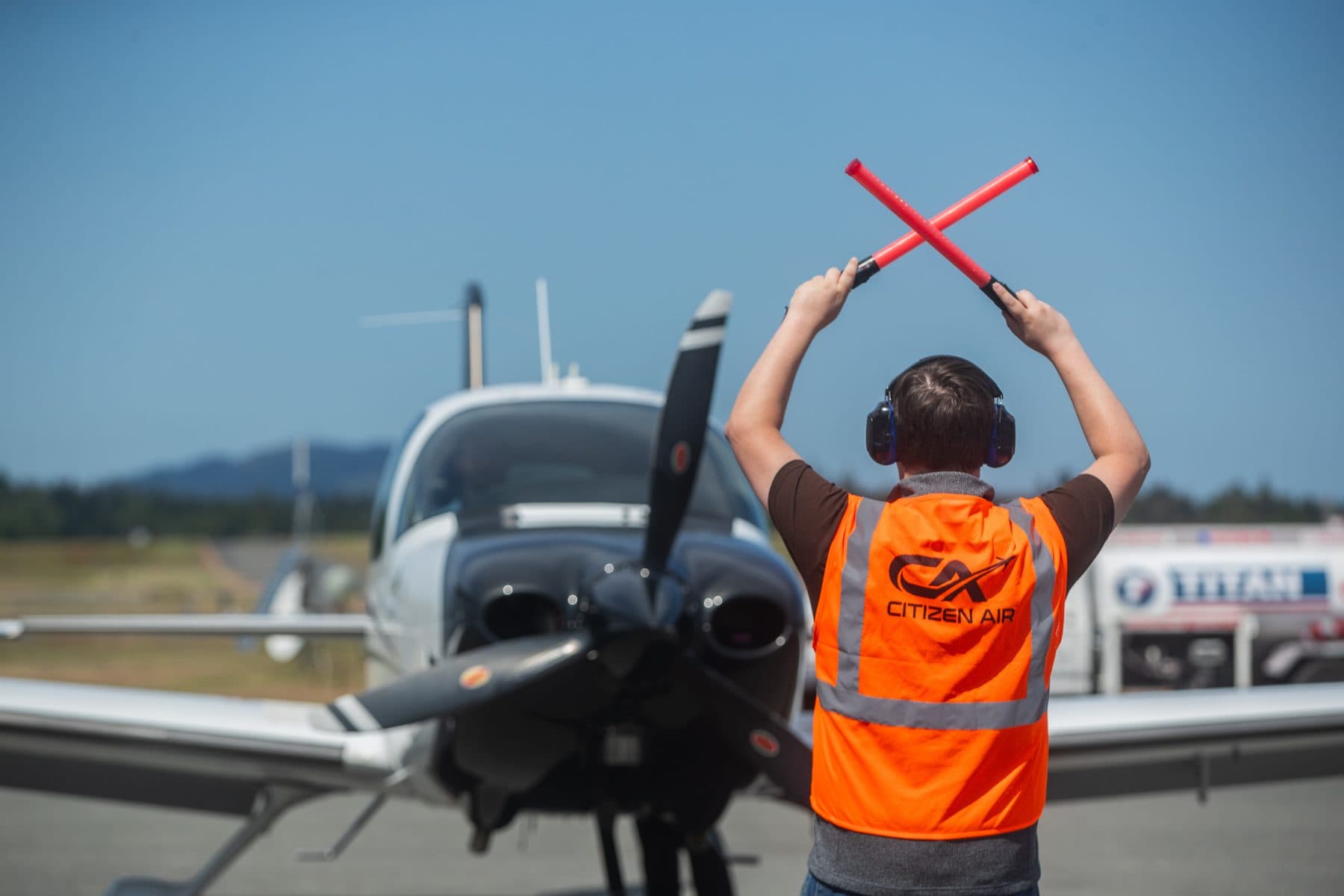 A Citizen Air line technician signaling stop with crossed marshalling wands in front of a Cirrus SR22 on the ramp