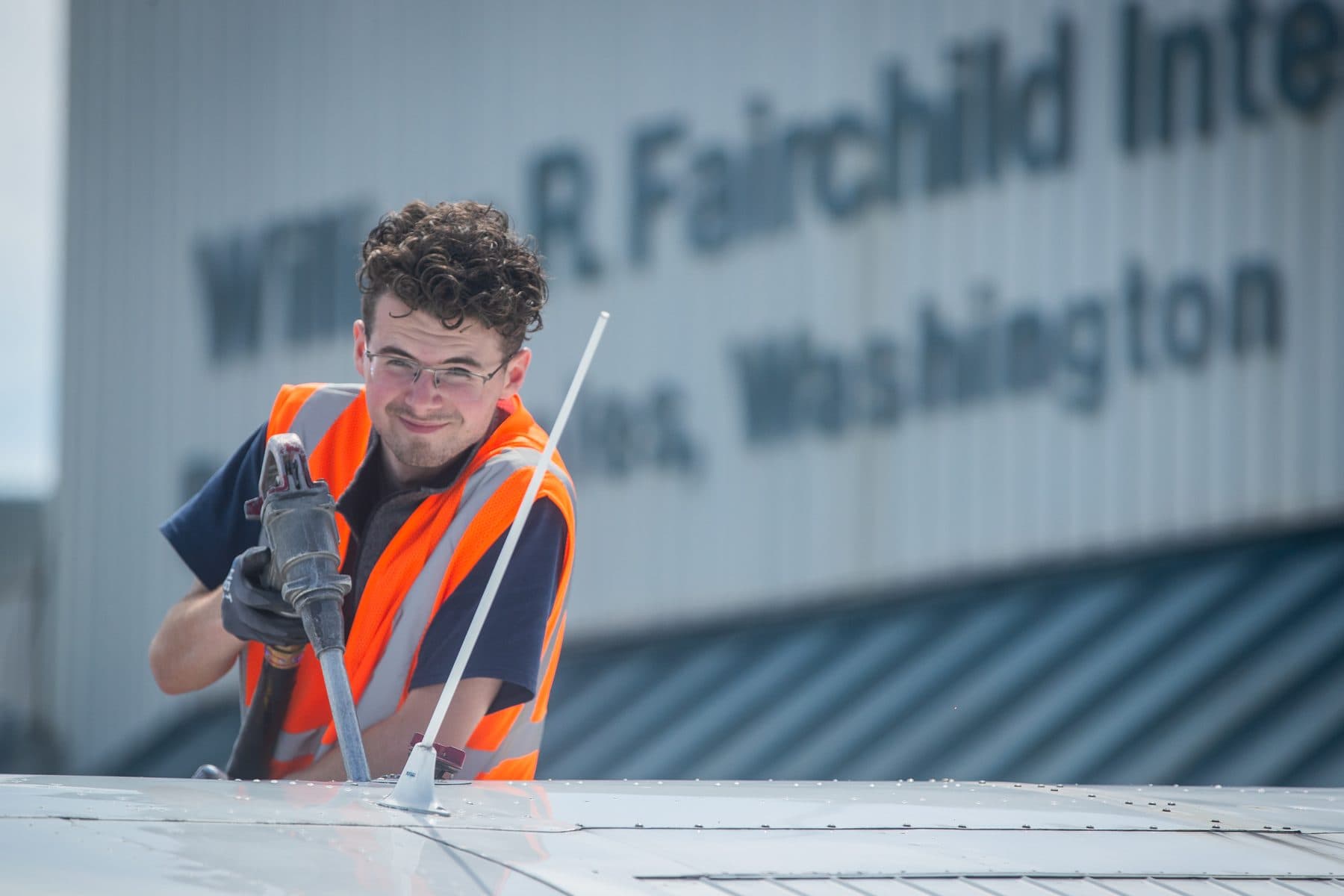 A line technician fueling a high-wing aircraft at the wing, the terminal sign behind him