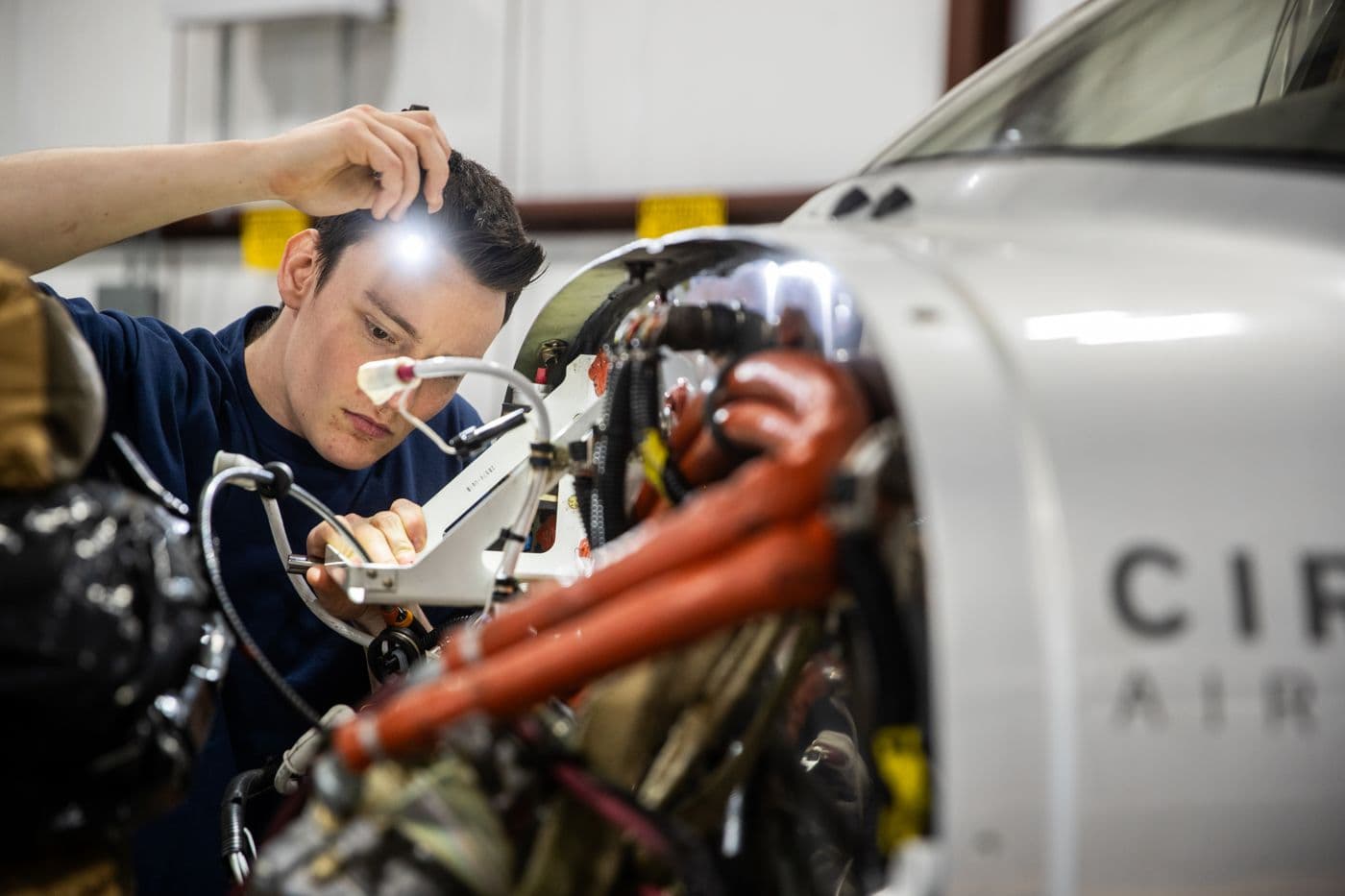 A Citizen Air technician inspecting the engine of the Cirrus SR22 with a headlamp