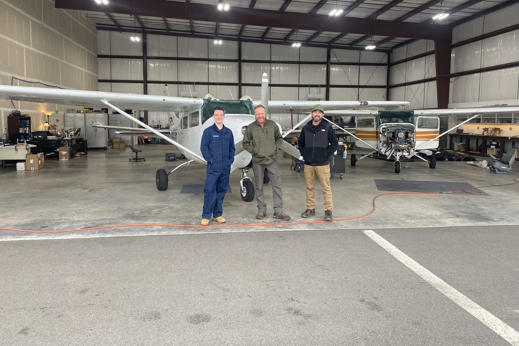 Three members of the Citizen Air maintenance team in the hangar, a Cessna 172 and 206 behind them