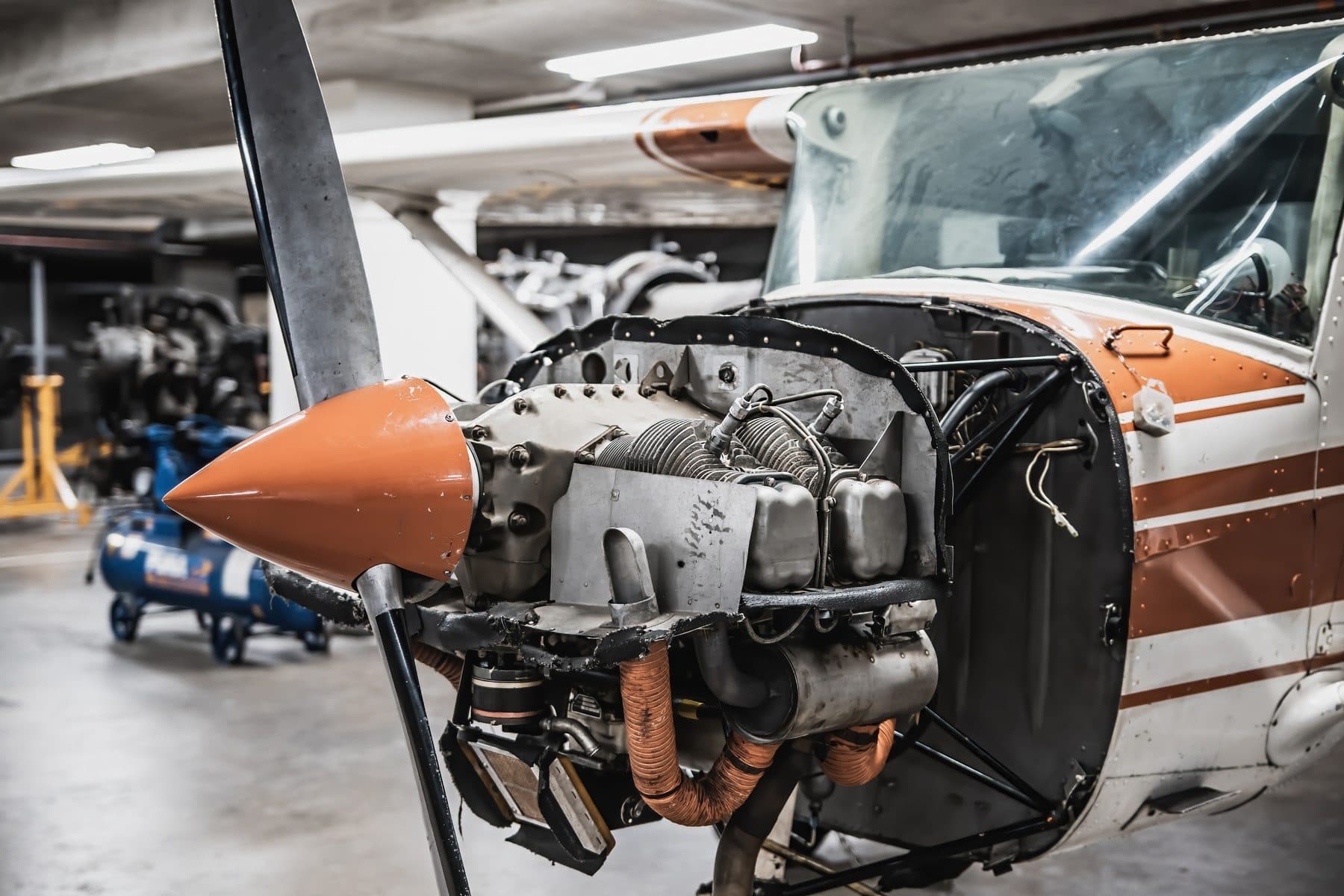 A Cessna with its cowling removed in a maintenance hangar, the engine open for inspection