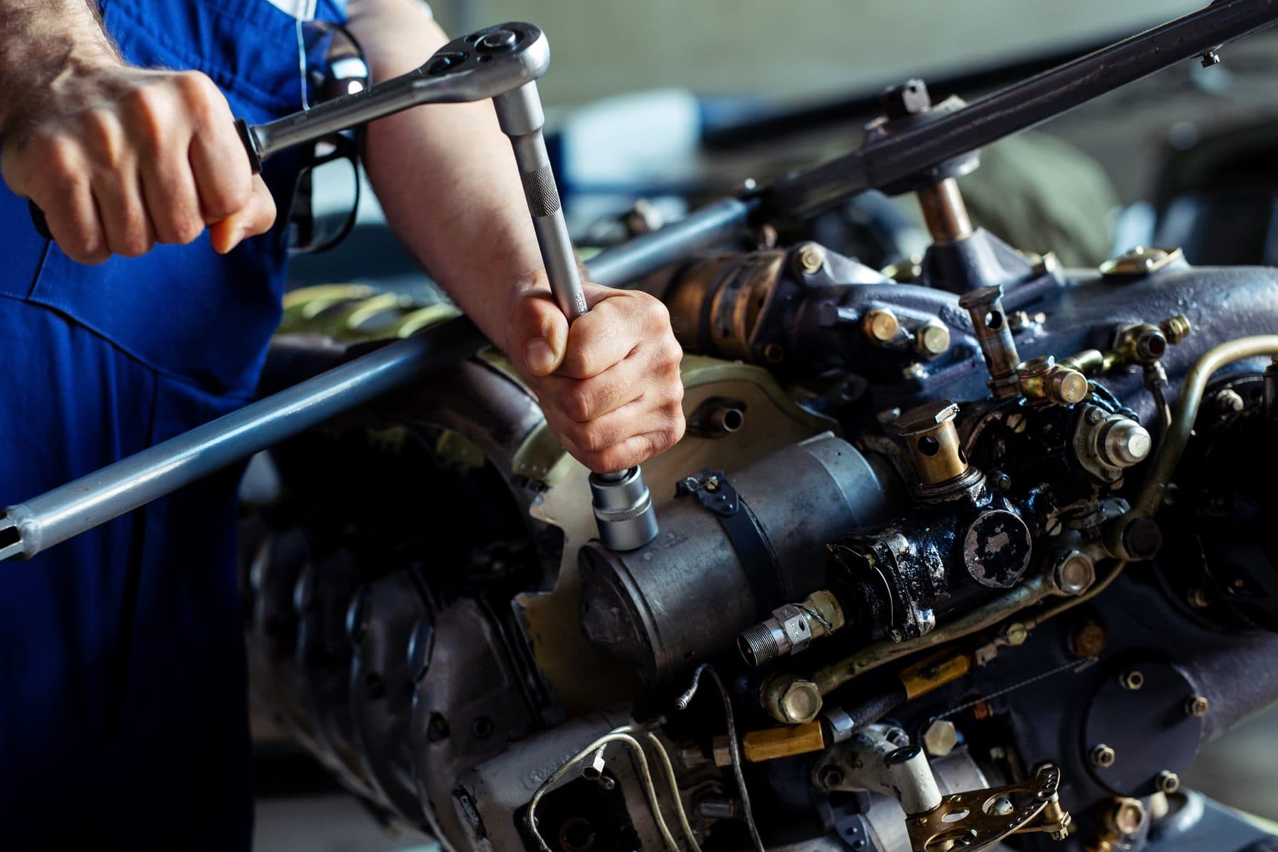 A technician working on a piston aircraft engine with a ratchet