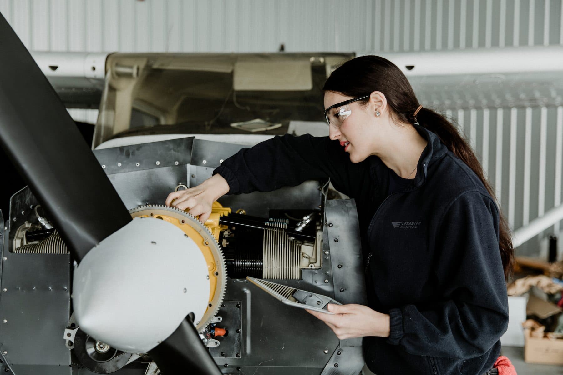 A technician inspecting the engine of a single-engine aircraft in the hangar, tablet in hand